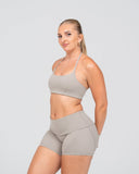 Woman wearing a beige sports bra and shorts set on a light gray background