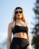 Woman wearing a black sports bra and leggings with sunglasses and a headband outdoors.