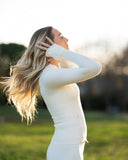 Woman in a white long-sleeve top and skirt standing in a field with a blurred background