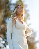 Woman in a white outfit standing outdoors with trees in the background