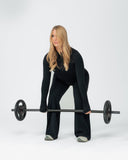 Woman in black outfit holding a barbell on a white background