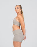 Woman wearing a beige sports bra and shorts set on a light gray background