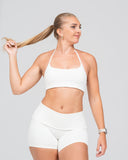 Woman wearing a white sports bra and high-waisted shorts on a light gray background
