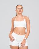 Woman wearing a white sports bra and shorts on a light gray background