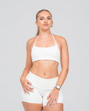 Woman wearing a white sports bra and shorts on a light gray background