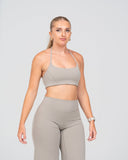 Woman wearing a beige sports bra and leggings on a gray background